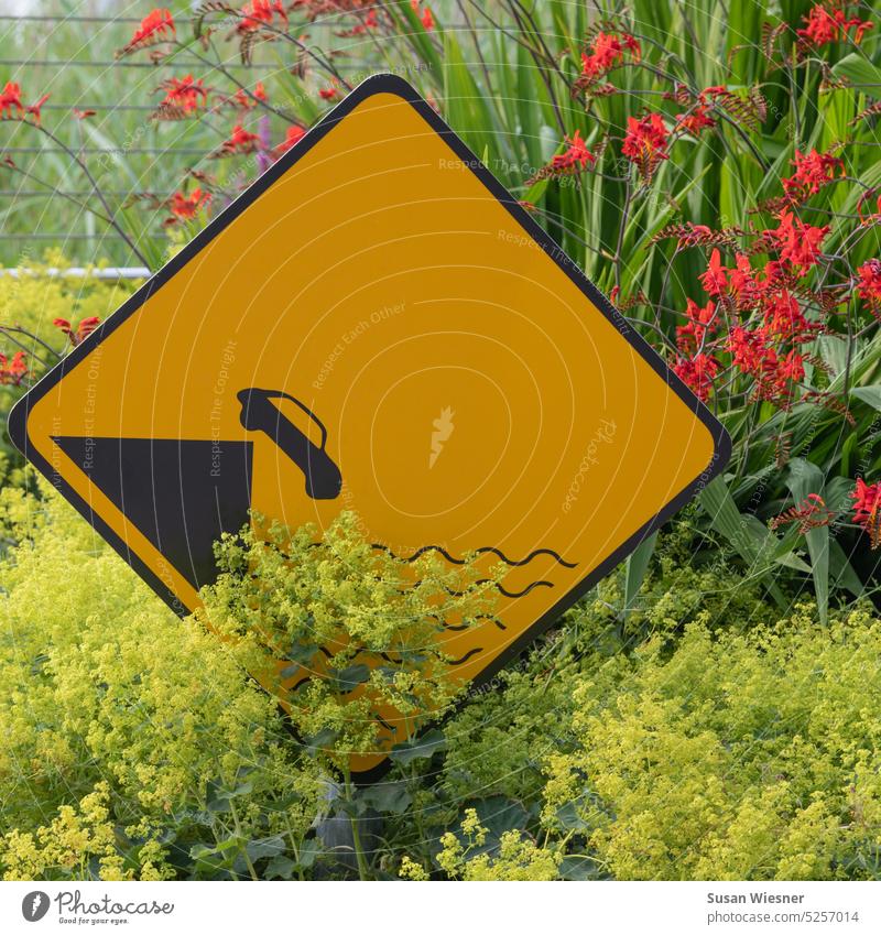 Gelbes Verkehrsschild zur Warnung vor ins Wasser stürzendes Auto in gelben und roten Blumen Verkehrszeichen Außenaufnahme Warnschild Absturzgefahr