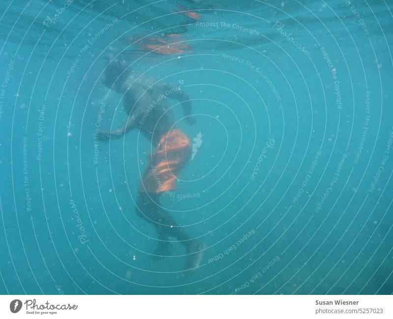 Person mit oranger Badeshorts unter türkisblauem Wasser schwimmend. unter Wasser Natur Mann abtauchen im Meer