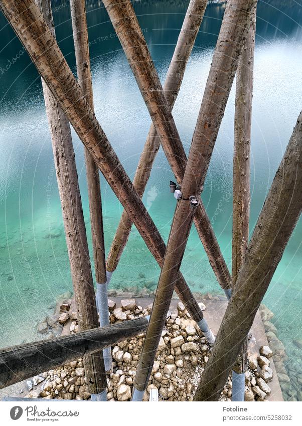 Die Holzbalken eines Aussichtsturms am See. Das Wasser ist klar und kalt. Unten liegen viele Steine herum ruhig Seeufer Farbfoto nass Achensee Balken