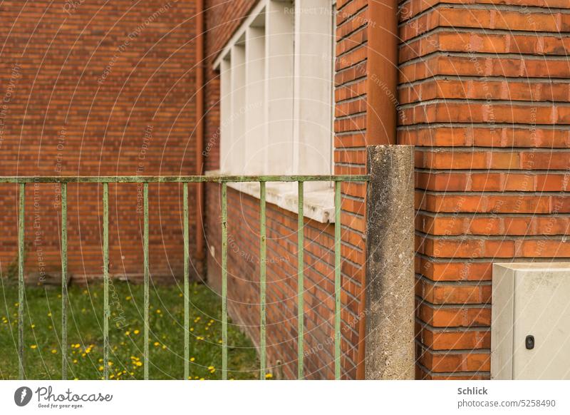 Backsteinarchitektur und Zaun aus Eisenstäben in grün Architektur Wiese Fenster Stromkasten Betonpfosten rot braun weiß regenfallrohr Zentralperspektive