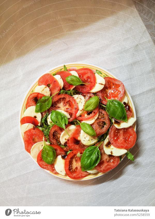 Draufsicht auf einen Teller mit frischem italienischem Caprese-Salat aus Tomaten, Mozzarella und Basilikumblättern, angemacht mit Balsamico-Essig und Olivenöl