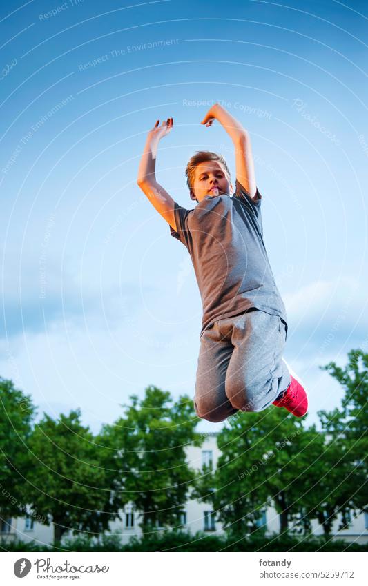 Junge springt hoch Gefedert Springen aktiv allein Außenaufnahme Luftsprung Bewegung Blick in die Kamera im Freien freudig passen Fitness sportlich