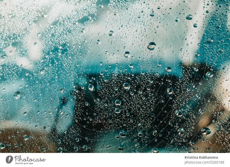 Blick auf Wassertropfen, die auf Glas fallen. Regen läuft am Fenster herunter. Regnerische Jahreszeit, Herbst. Regentropfen rieseln herunter, blauer Himmel.