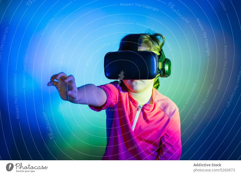Mädchen erlebt VR-Headset Spiel auf bunten blauen Hintergrund Kind berühren unsichtbar Objekt Schutzbrille futuristisch Cyberspace Anschluss unterhalten