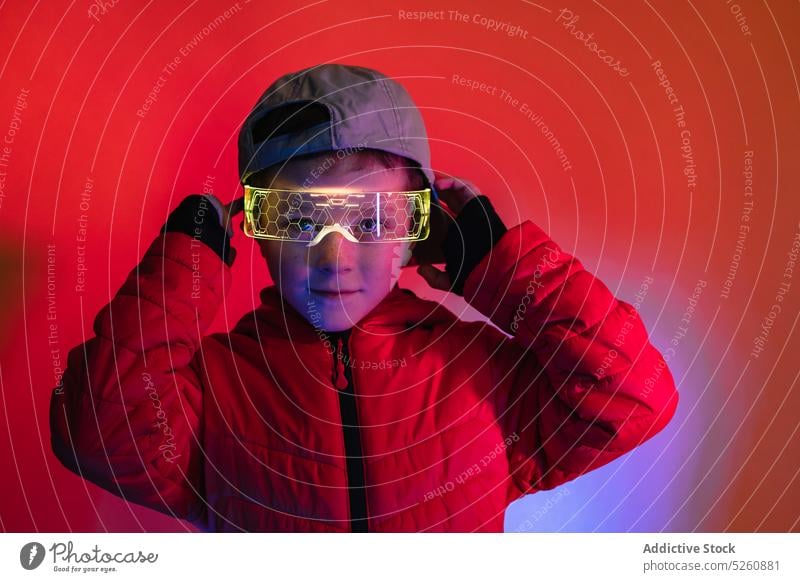 Junge, der eine futuristische digitale Schutzbrille einstellt ausrichten leuchten neonfarbig Cyberpunk farbenfroh hell modern Stil glühen Brille Kind