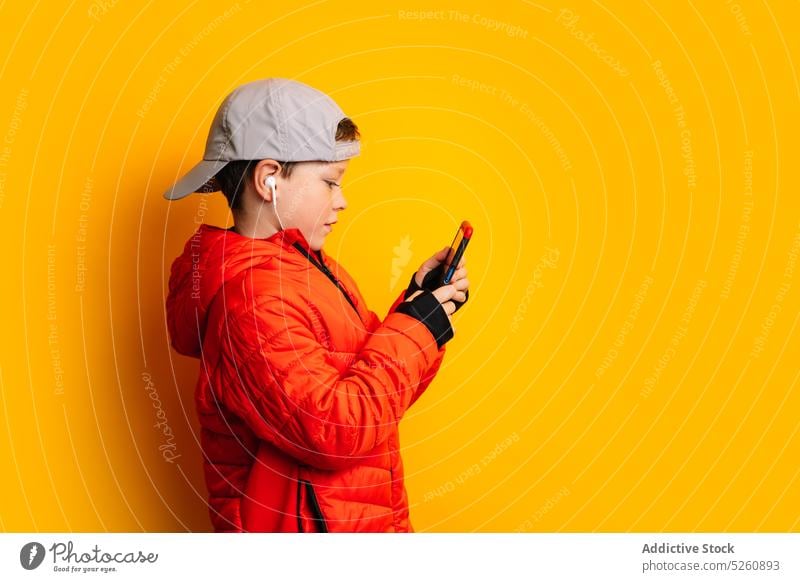 Junge benutzt Smartphone und hört Musik über Kopfhörer Kind benutzend zuhören Apparatur Studioaufnahme Wiedergabeliste Gesang Browsen Surfen Internet Drahtlos