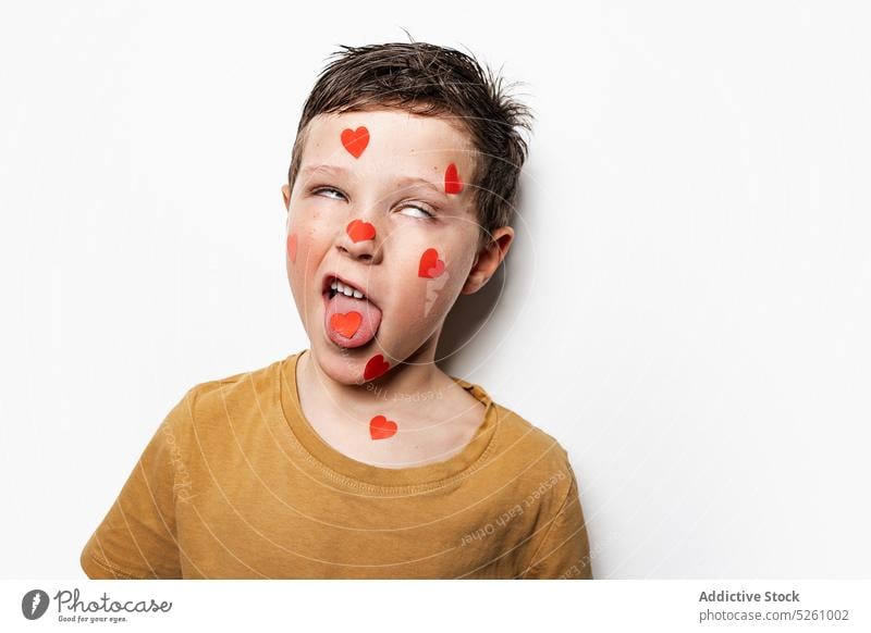 Lustiger Junge mit Herzen im Gesicht Zunge zeigen lustig Gesicht machen mit den Augen rollen Valentinstag (Heiliger Valentinstag) Feiertag Liebe Kindheit