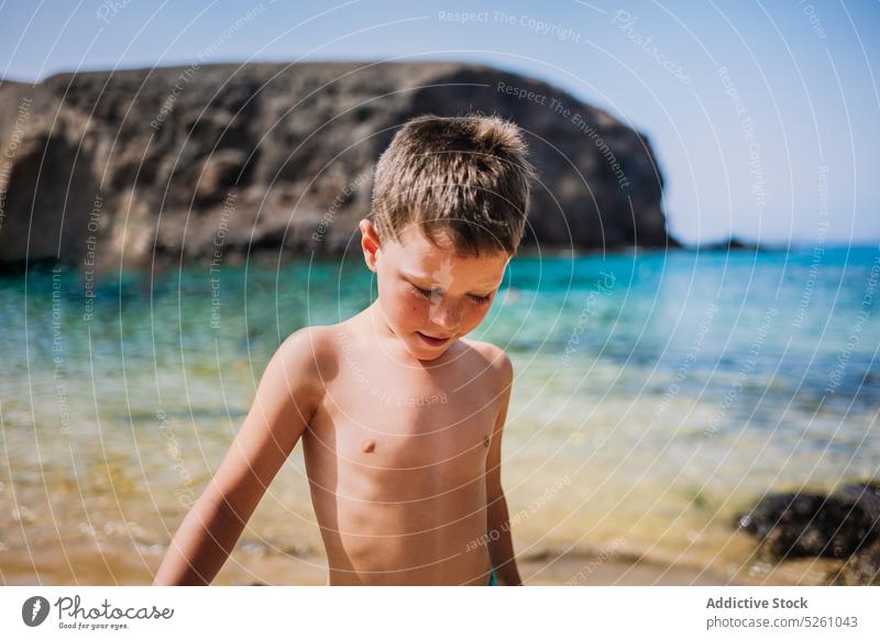Junge in Badehose am Strand stehend Kind MEER Wasser Ufer Natur wolkenlos Sommer Feiertag Resort Lanzarote Papageienstrand Spanien Europa Urlaub Tageslicht