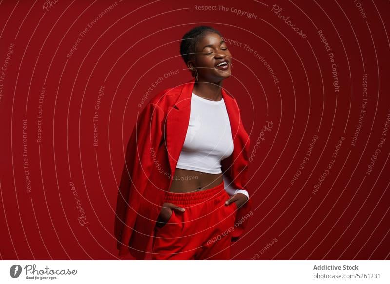 Stilvolle afroamerikanische Frau steht in der Nähe der roten Wand Model Hochmut Hand-in-Tasche selbstbewusst Vorschein Outfit Individualität Jacke ethnisch cool