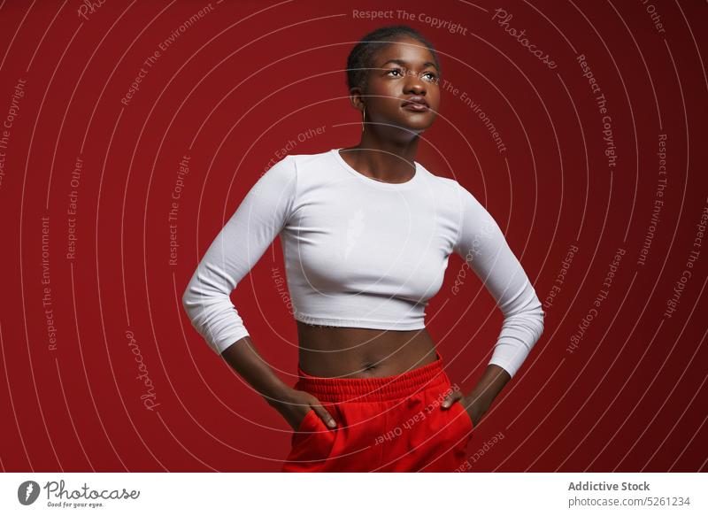 Stilvolle afroamerikanische Frau steht in der Nähe der roten Wand Model Hand-in-Tasche selbstbewusst Vorschein Outfit Individualität ethnisch cool
