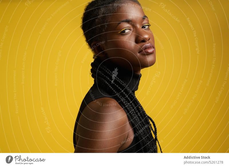 Ernste afroamerikanische Frau in der Nähe der gelben Wand Hochmut Make-up lebhaft hell Frisur Geflecht Stil Vorschein Mode ethnisch Top cool selbstbewusst ernst