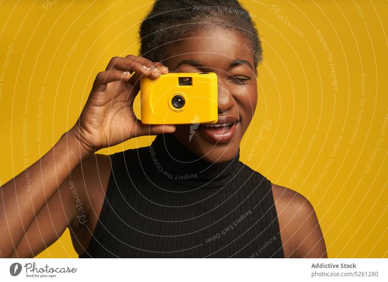 Fröhliche afroamerikanische Frau mit Retro-Kamera auf gelbem Hintergrund heiter fotografieren Fotoapparat retro Fotografie einfangen lebhaft hell Hobby Moment