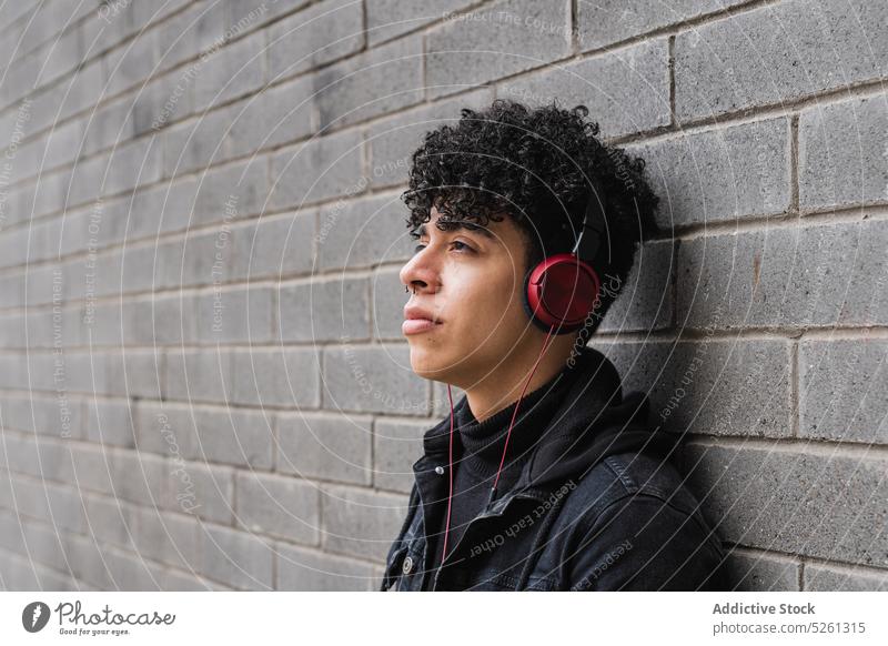 Stylische lateinamerikanische Migrantin, die mit Kopfhörern Musik hört Mann Schüler zuhören Backsteinwand Gebäude Wiedergabeliste Straße Typ hispanisch ethnisch