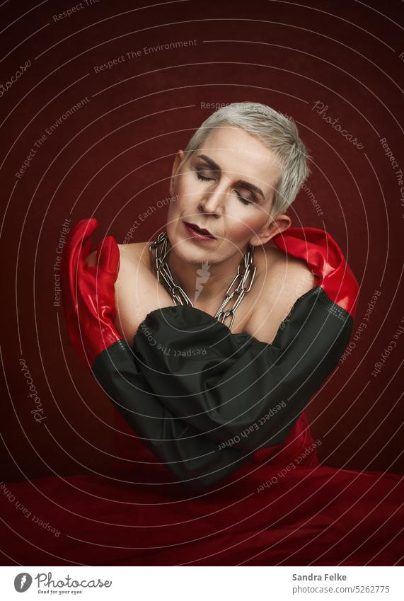 Portrait einer Frau mit geschlossenen Augen. Sie trägt eine Kette aus schwerem Metall und Gummihandschuhe. Metallkette portrait feminin nachdenklich rot