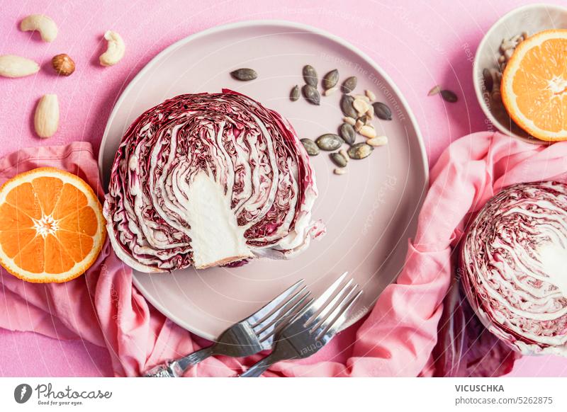 Halbierter Radicchio mit Salatzutaten auf einem Teller mit rosa Tischhintergrund, Ansicht von oben. Gesundes Essen Konzept halbiert Hintergrund Draufsicht