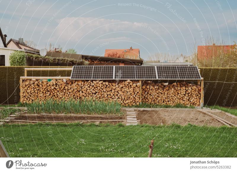 Eigenanbau Gemüse und Holzvorrat mit Brennholz unter Solarplatten im Garten Photovoltaik Solarpanele Nachhaltigkeit nachhaltiger Lebensstil