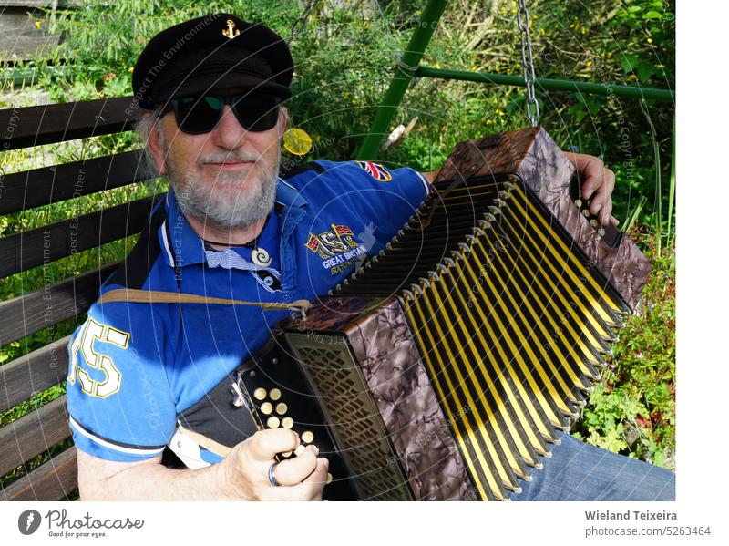 Älterer Mann mit Kapitänsmütze sitzt draußen und spielt ein diatonisches Knopfakkordeon Gesicht Person Musikinstrument altehrwürdig im Freien männlich