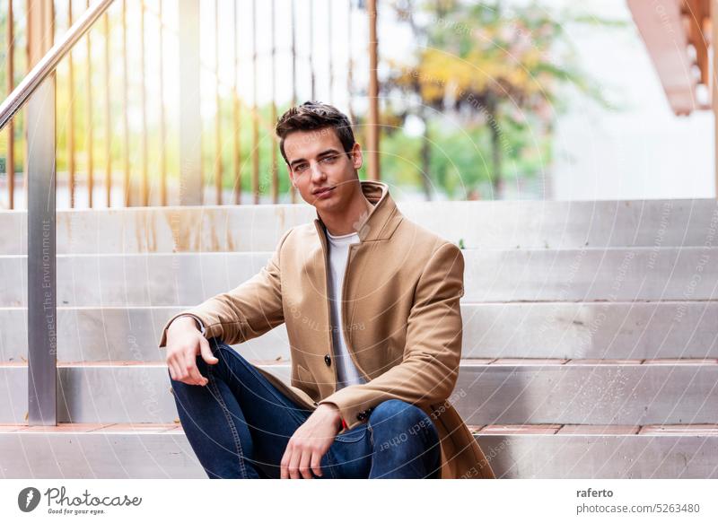 Porträt eines stilvollen, gut aussehenden jungen Mannes mit Mantel, der im Freien sitzt Erwachsener Fotokamera Kaukasier Selbstvertrauen Eleganz Inspiration