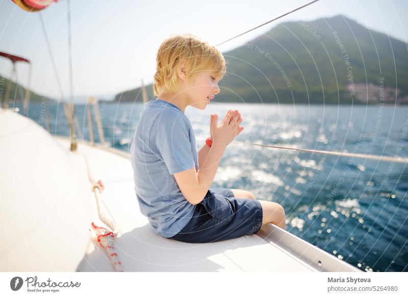 Kleiner Junge an Bord eines Segelbootes in der Bucht von Boka Kotor an der Adria im Balkangebirge, Montenegro, Europa. Glückliches Kind auf einer Seereise während der sonnigen Sommerferien Tag.