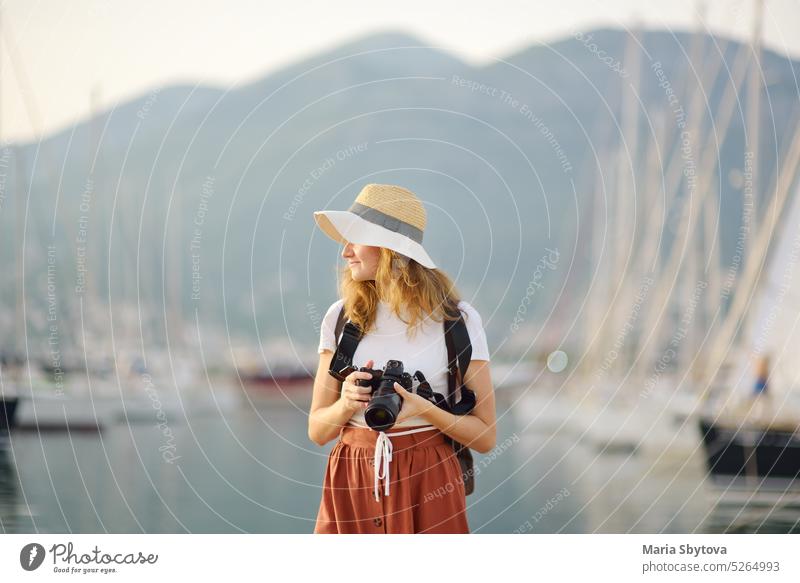 Charmante junge Touristin, die ein Foto an der Mittelmeerküste macht. Attraktive rothaarige Mädchen Fotograf mit einer Kamera auf dem Hintergrund von Meer und Yachten. Tourismus und Reisen