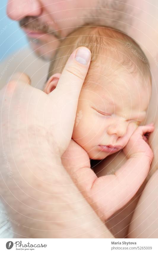 Reifer Vater hält sein süßes neugeborenes Baby. Das Baby schläft in den Armen des Vaters. Papa Haut-an-Haut Kontakt Säugling Halt Vaterschaft Beteiligung