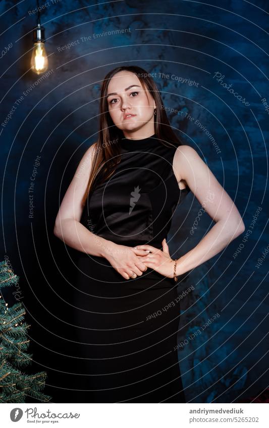 junge schöne Frau in einem schwarzen festlichen langen Kleid in der Nähe des Weihnachtsbaums. Elegante Dame im schwarzen Kleid über Weihnachtsbaum Lichter Hintergrund. frohes neues Jahr
