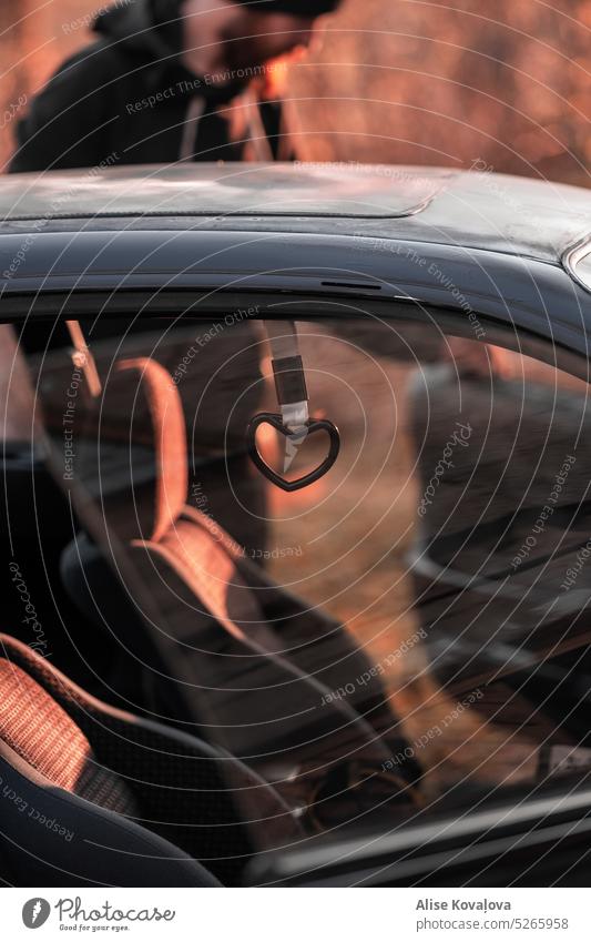 Kunststoffherz Autoinnenraum PKW Autofenster Detailaufnahme Farbfoto Reflexion & Spiegelung Sonnenuntergangslicht Herzanhänger aus Kunststoff herzförmig schwarz