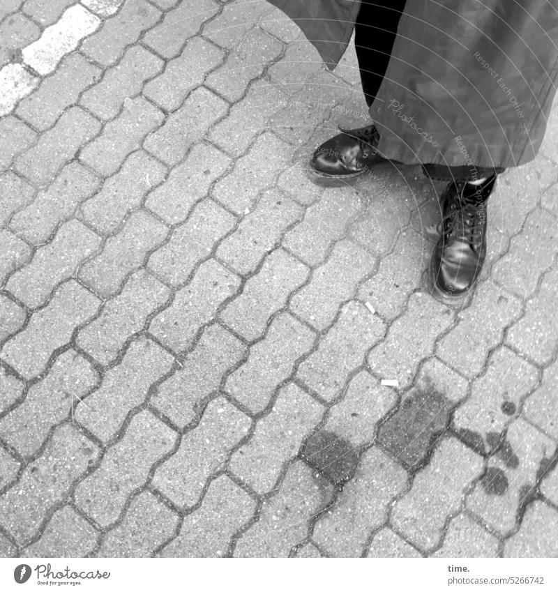 Frau im Mantel neben Ölfleck auf gepflastertem Untergrund Pflasterung Gehweg Stein Stiefel stehen Fleck angewinkelt Muster Struktur Vogelperspektive