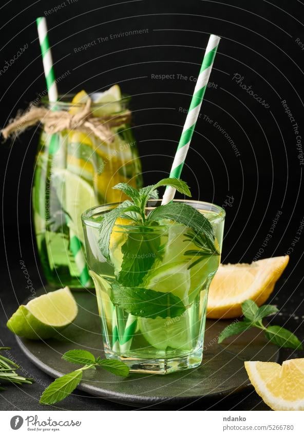 Limonade in einem transparenten Glas mit Zitrone, Limette, Rosmarinzweigen und Minzblättern auf schwarzem Hintergrund Kalk trinken Cocktail Erfrischung Frucht