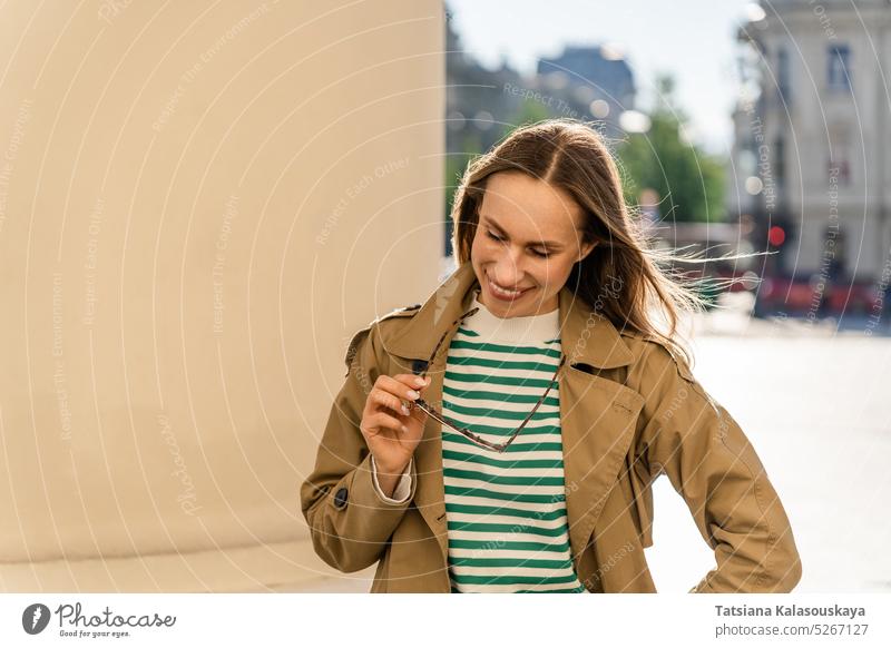 Eine Frau lächelt und hält eine Sonnenbrille in der Hand, während sie durch die Stadt geht Glück Fröhlichkeit heiter Freude Erwachsener jauchzen midlife