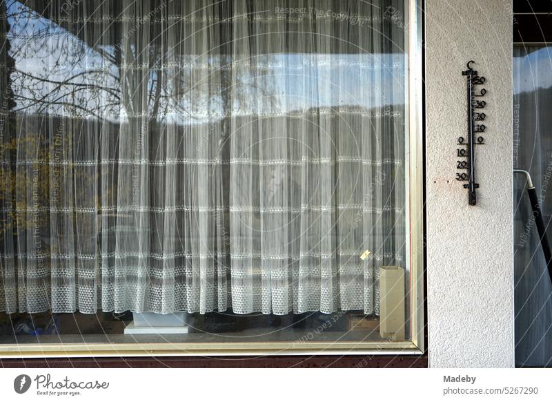 Gardine in einem alten Fenster mit Rahmen aus Messing und Außenthermometer einer ehemaligen Tankstelle in Beige und Naturfarben am Edersee bei Waldeck im Landkreis Waldeck-Frankenberg in Hessen