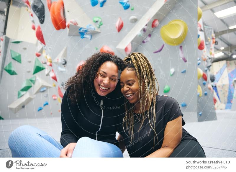 Zwei lächelnde Freundinnen haben Spaß beim Lachen, als sie die Kletterwand im Indoor-Aktivitätszentrum ausprobieren Frauen Freunde Aufsteiger Klettern Zentrum