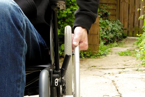 Eine behinderte Person in einem Rollstuhl. Ein Mann mit eingeschränkter Mobilität in einer begrünten Gasse. allein Behinderungen im Freien Hand Rad abschließen