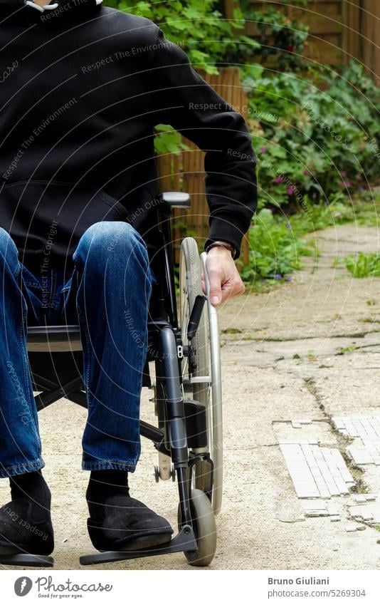 Eine behinderte Person in einem Rollstuhl. Ein Mann mit eingeschränkter Mobilität auf einem Weg mit Vegetation. allein Behinderungen im Freien Einsamkeit