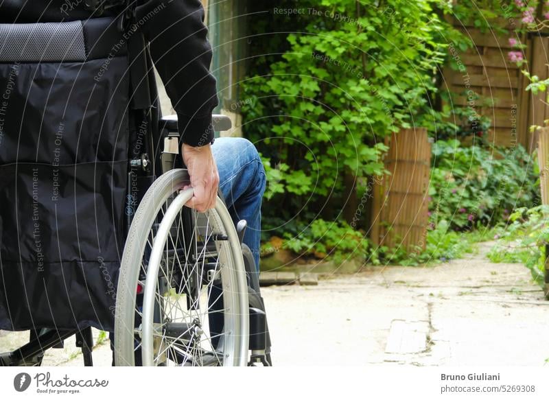 Eine behinderte Person in einem Rollstuhl. Ein Mann mit eingeschränkter Mobilität auf einem Weg mit Vegetation. Behinderung Personen mit Behinderungen