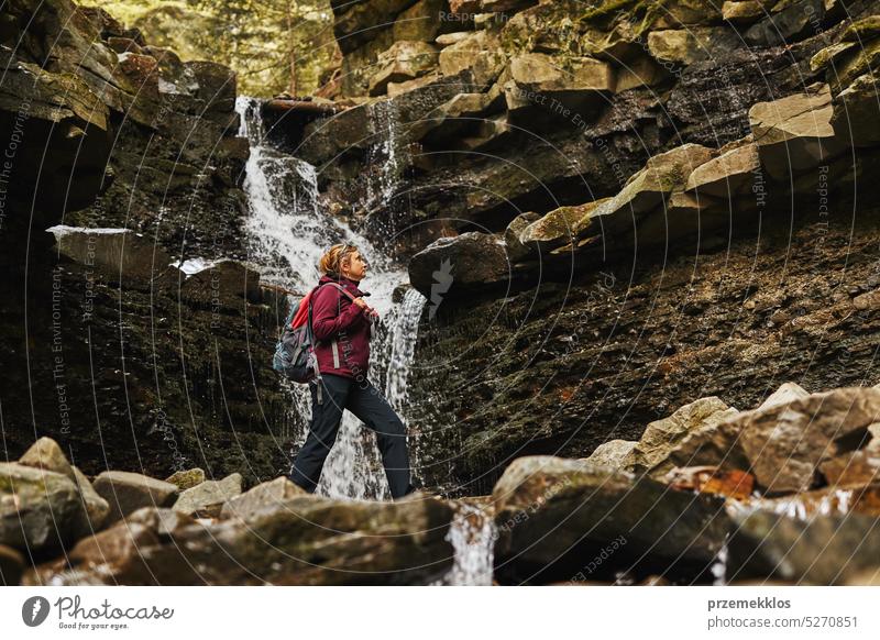 Wandern in den Bergen. Frau genießt Wanderung am sonnigen Urlaubstag. Frau mit Rucksack zu Fuß in der Nähe von Wasserfall. Verbringen Sommerurlaub in der Nähe der Natur