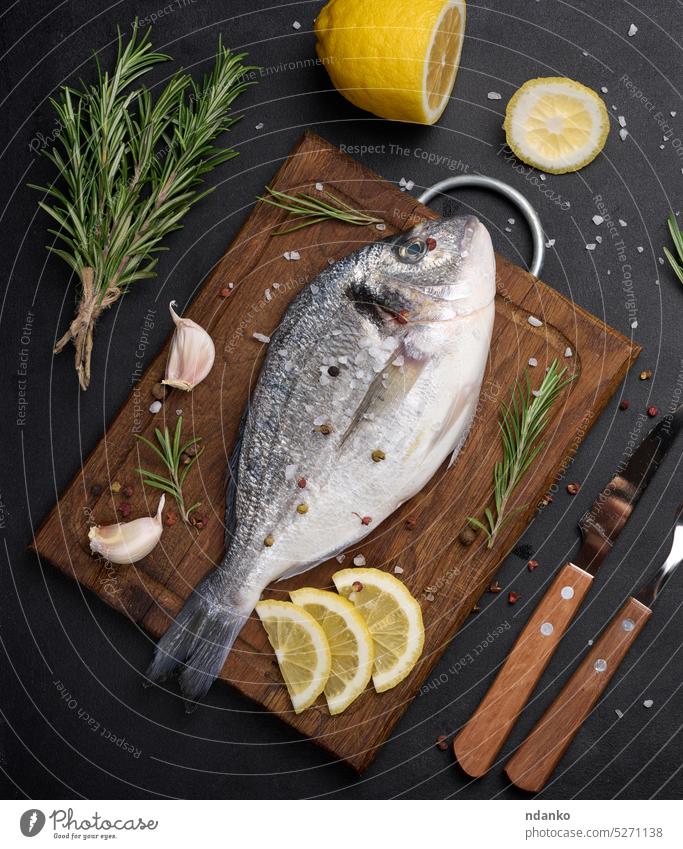 Roher ganzer Goldbrassenfisch auf Küchenbrett und Gewürzen zum Kochen, Draufsicht auf schwarzen Tisch roh Dorado Fisch Meeresfrüchte Essen zubereiten Rosmarin