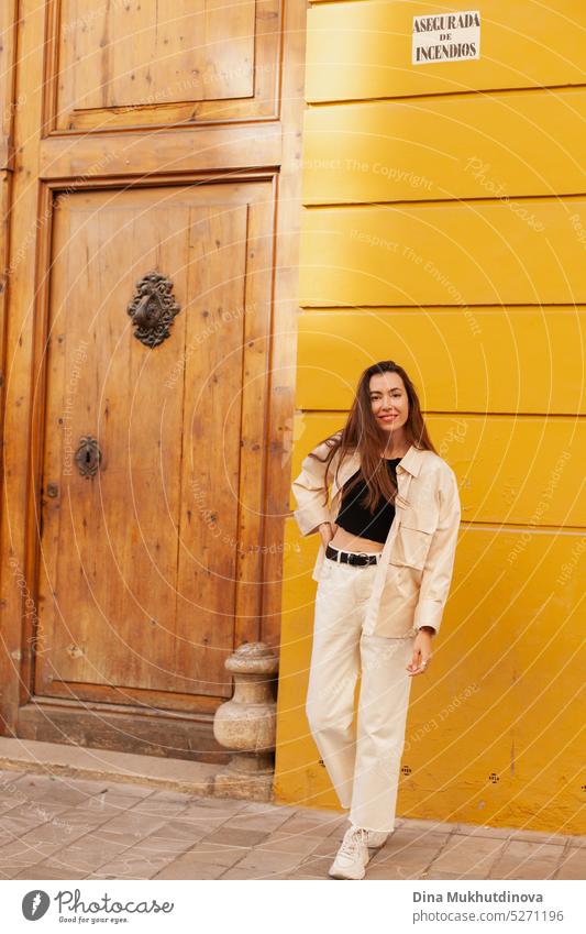 Junge Frau steht in der Nähe einer gelben Wand und einer braunen Holztür und schaut in die Kamera tausendjährig urban Model Großstadt Tourist Tourismus jung