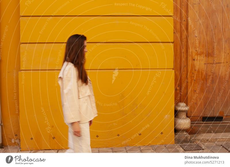 Junge Frau geht an einem gelben Gebäude vorbei. Bewegungsunschärfe Bild. Person in Bewegung in der Stadt. tausendjährig urban Model Wand Großstadt Tourist