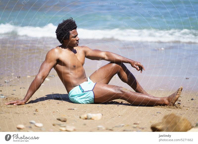 Schwarzer Mann im Badeanzug sitzt am Sandstrand Strand MEER Meeresufer Sommer Urlaub sich[Akk] entspannen Feiertag Wasser Wochenende männlich ethnisch