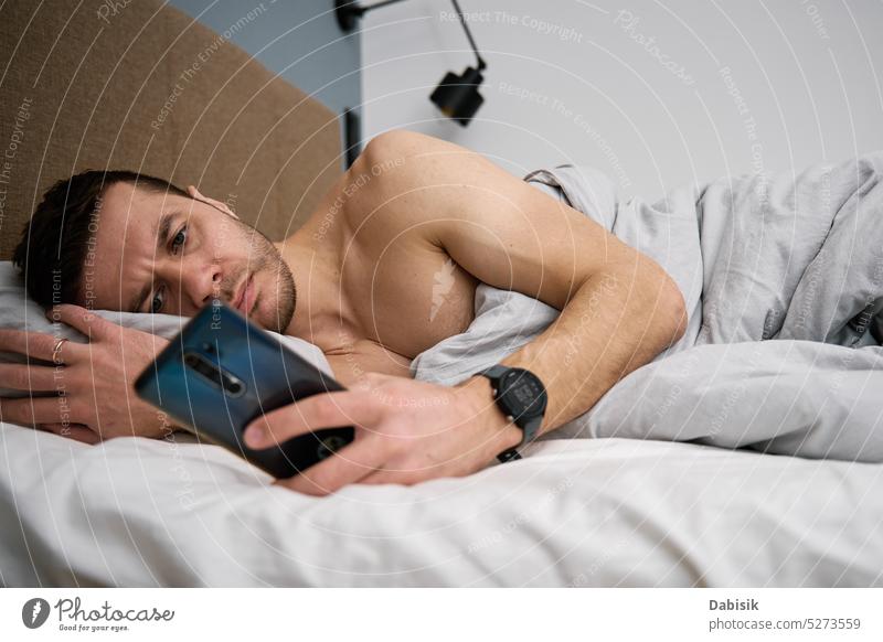 Handy-Sucht. Mann im Bett liegend mit Smartphone Lügen Telefon Schlafzimmer Lifestyle Browsen Morgen Freizeit Funktelefon online aussruhen Decke
