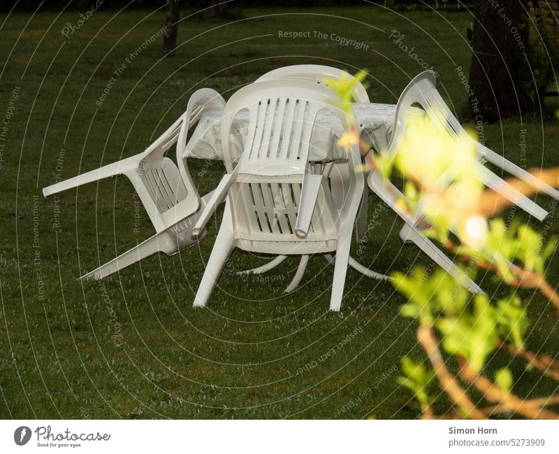 Tisch mit angelehnten Monobloc-Stühlen stehen auf einer Rasenfläche Gartenmöbel Plastik Regen regnerisch Sommerregen Dämmerung draußen Konferenz Urlaub Design