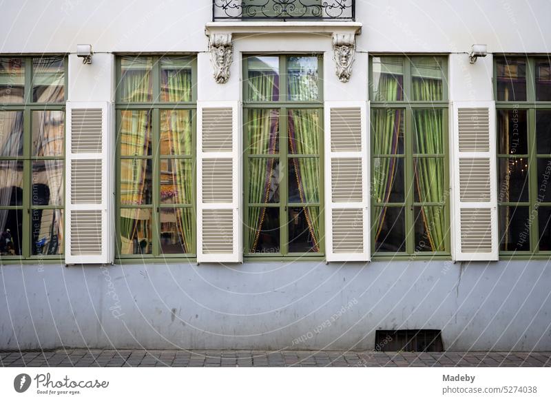 Schöne grüne alte Fenster mit farblich passenden Vorhängen und Fensterläden aus Holz mit Lamellen eines sanierten Altbau in der Altstadt von Gent in Ostflandern in Belgien