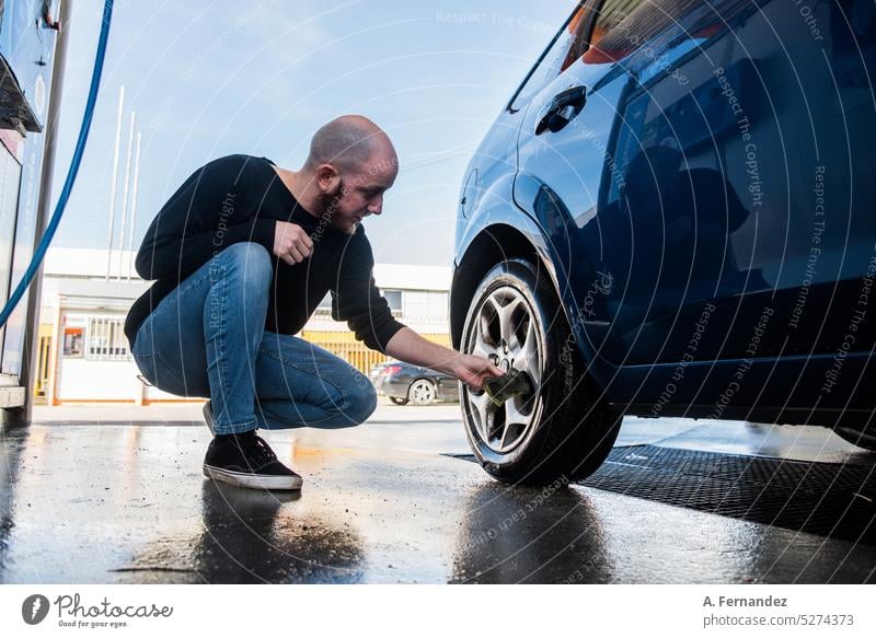 Junger Mann reinigt den Reifen seines Autos mit einem Schwamm in einer Autowaschanlage Autowäsche Reinigen Sauberkeit dreckig PKW Waschen Wasser Schmutz