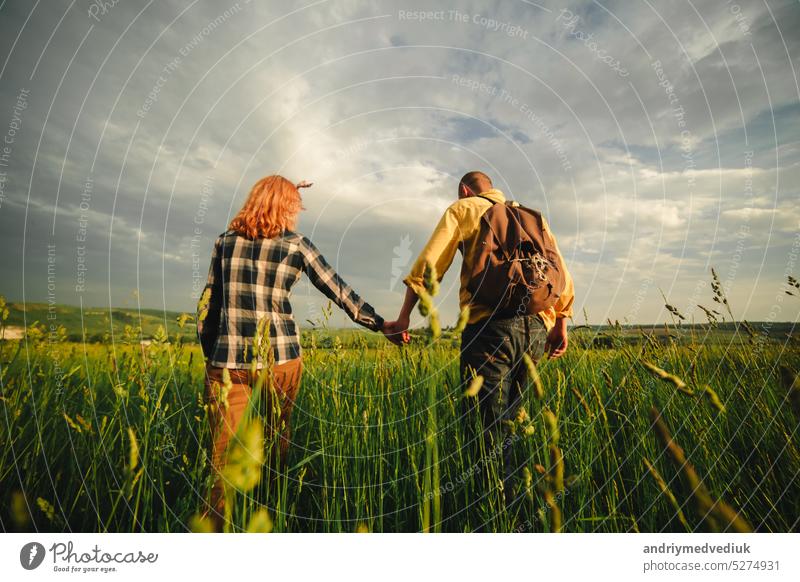 Verliebtes Hipster-Paar, das im Feld spazieren geht, sich küsst und die Hände hält, sich umarmt, im Sommer bei Sonnenuntergang im Gras liegt. valentines day