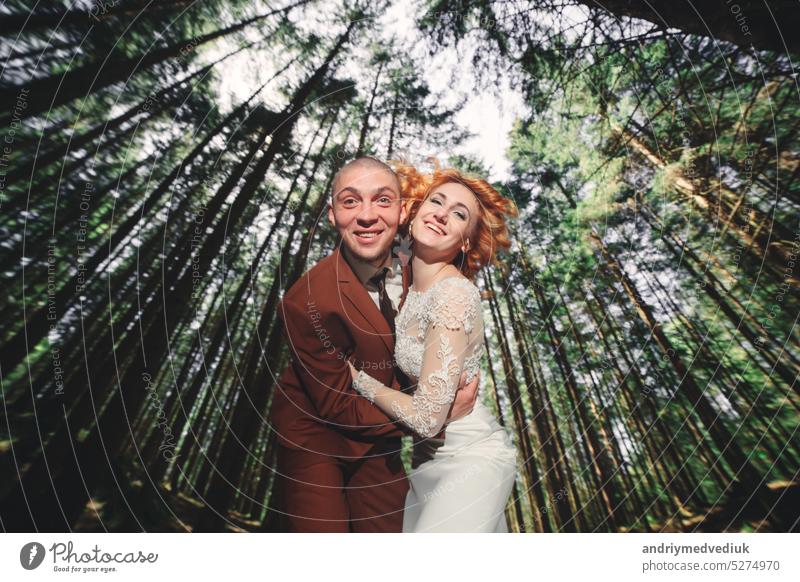 Glückliche stilvolle Paar Jungvermählten in den grünen Wald am Sommertag. Braut in langen weißen Kleid und Bräutigam im roten Anzug sind umarmt. Park Tag