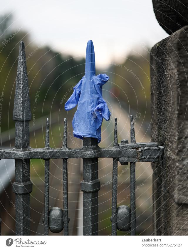 Einweg-Handschuh auf Eisengitter streckt Mittelfinger aus Einweghandschuh Beleidigung Stinkefinger ausgestreckt austrecken Gitter Geländer blau Müll Kunststoff
