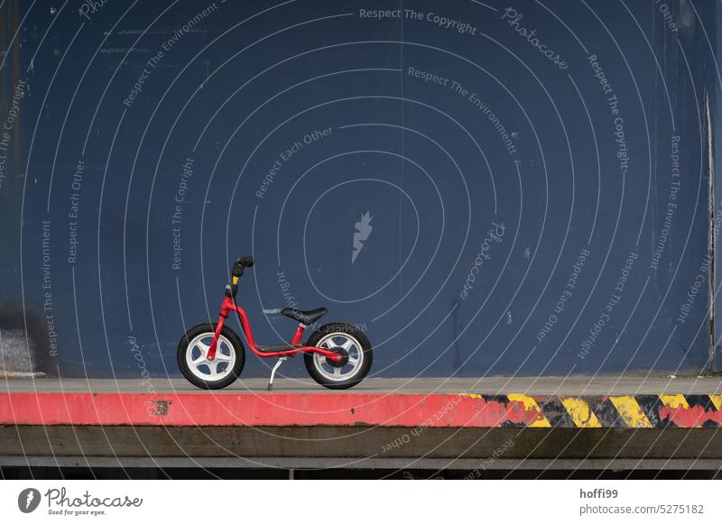rotes Laufrad auf Rampe minimalistisch Kinderrad kinderlaufrad Fahrrad Fahrradfahren Kindheit Rad Mobilität Fassade grau umweltfreundlich Lifestyle