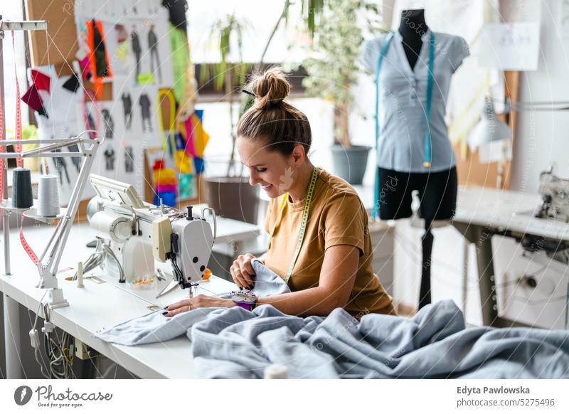 Modedesignerin an einer Nähmaschine an ihrem Arbeitsplatz Handwerk Schneidern Herstellung handgefertigt Näherin Kleinunternehmen Werkstatt Gewebe Hobby Nähen