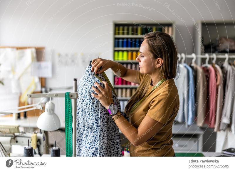 Junge Modedesignerin bei der Arbeit an ihrem Arbeitsplatz Handwerk Schneidern Herstellung handgefertigt Näherin Kleinunternehmen Nähmaschine Werkstatt Gewebe
